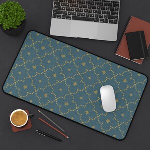 Op de afbeelding: Een rechthoekige teal muismat met een zwarte rand en een herhalend patroon van gouden sterren en stippen. Een witte computermuis ligt op de mat, met een laptop, notitieboekjes en een kopje koffie in de buurt.
