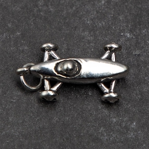 May include: A silver charm in the shape of a race car with four wheels and a single driver. The charm has a loop at the top for attaching to a bracelet or necklace.