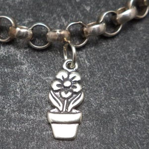May include: A silver chain necklace with a silver charm of a potted flower.