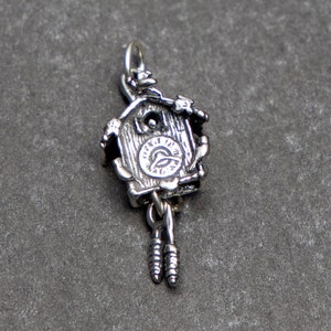 May include: Silver charm in the shape of a cuckoo clock with a detailed design and a swinging pendulum.