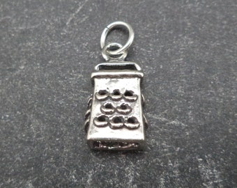 May include: A silver charm in the shape of a grater. The charm is detailed with a textured surface and a loop for attaching to a bracelet or necklace.