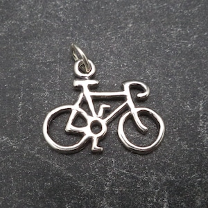 Op de afbeelding: Een zilveren bedel in de vorm van een fiets. De bedel is een eenvoudige omtrek van een fiets met twee wielen, een stuur en een zadel.