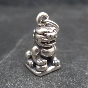 May include: Silver charm featuring a detailed sculpture of a Foo Dog, a mythical lion-like creature often used as a guardian in Chinese culture.