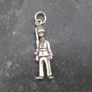 May include: Silver charm of a soldier in a traditional uniform, holding a rifle. The charm has a loop at the top for attaching to a bracelet or necklace.