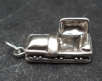 May include: A silver charm in the shape of a small, open casket. The charm has a hinged lid and a detailed design.