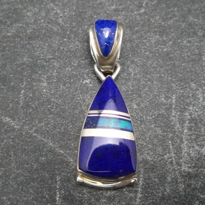 May include: A silver pendant featuring a teardrop-shaped lapis lazuli stone. The stone is surrounded by a silver border and has a thin silver band across the centre.