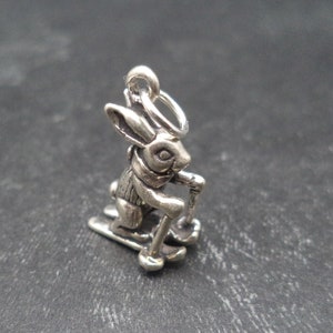 May include: A silver charm of a rabbit wearing a scarf and skiing down a slope.