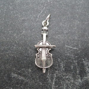 May include: A silver charm in the shape of a cello, a stringed musical instrument.