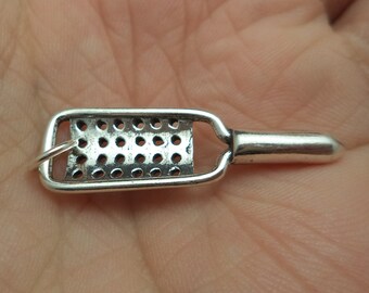 May include: A silver grater charm with a hole pattern and a loop for attaching to a necklace or bracelet.