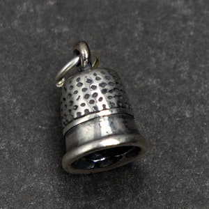 May include: A silver thimble charm with a textured surface.