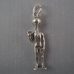 Peut inclure: Un charme en argent en forme d'extraterrestre humanoïde avec de grands yeux et une main levée. Le charme est attaché à une boucle en argent.