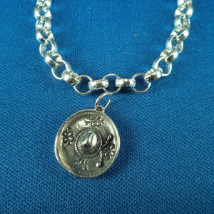 May include: A silver chain bracelet with a silver charm in the shape of a sombrero. The charm has a detailed design with a flower pattern.