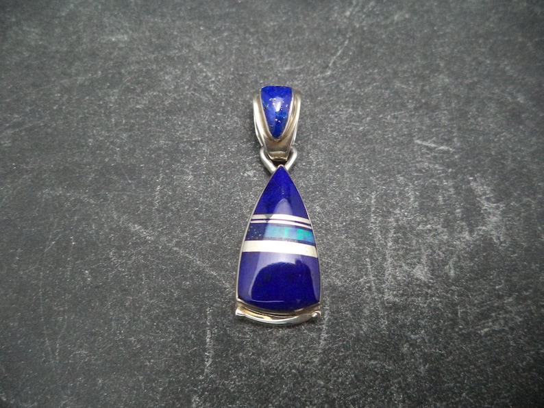 May include: A silver pendant featuring a teardrop-shaped lapis lazuli stone. The stone is surrounded by a silver border and has a thin silver band across the centre.