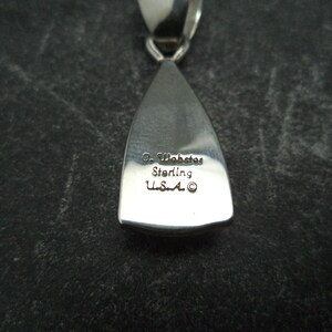May include: A silver pendant in the shape of a teardrop. The pendant is engraved with the text "C. Wabaste Sterling U.S.A."