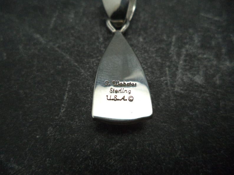 May include: A silver pendant in the shape of a teardrop. The pendant is engraved with the text "C. Wabaste Sterling U.S.A."
