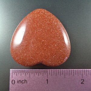May include: A heart-shaped red sandstone stone with a glittery texture. The stone is about 1 inch wide and 2 inches long.