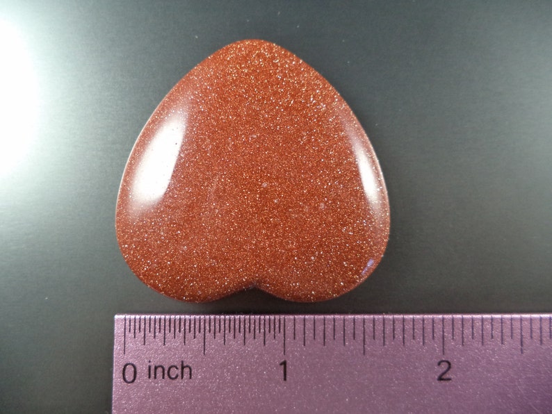 May include: A heart-shaped red sandstone stone with a glittery texture. The stone is about 1 inch wide and 2 inches long.