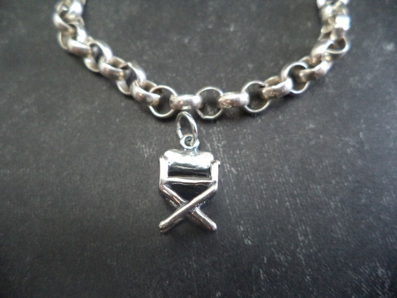 May include: A silver chain bracelet with a silver director's chair charm.