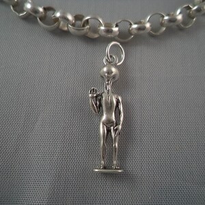 May include: A silver chain necklace with a silver alien charm. The alien is standing with one arm raised and is wearing a simple outfit.