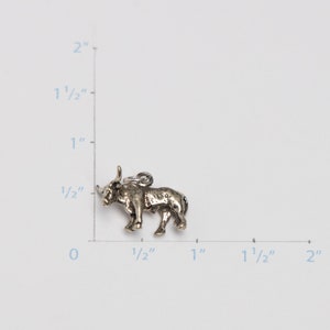 Puede incluir: Encanto de plata de un toro, de aproximadamente 2,5 cm de largo. El encanto est&aacute; detallado con una superficie texturizada y un cuerno en relieve.