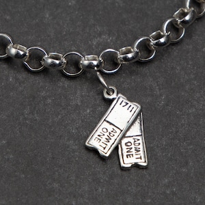 Puede incluir: Un brazalete de plata con un dije de billete de plata que dice "Admit One" en ambos lados. El dije est&aacute; unido a una cadena de plata.