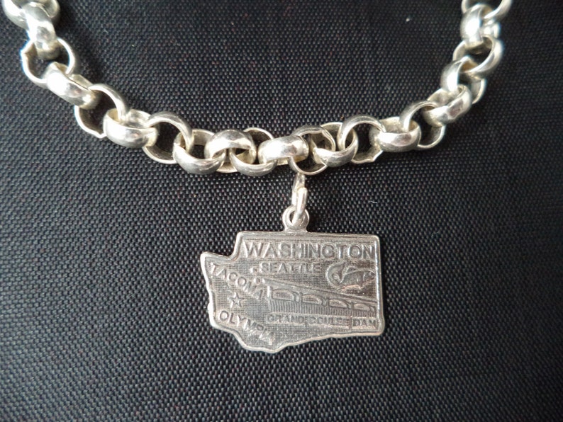 Op de afbeelding: Zilveren armband met een charme van de staat Washington met de tekst "WASHINGTON, SEATTLE, TACOMA, OLYMPIA, GRAND COULEE DAM".