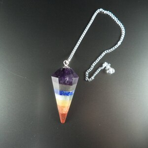Op de afbeelding: Een zeven-chakra kristallen slinger met een zilveren ketting. De slinger is een puntige, gefacetteerde kristal met lagen amethist, rookkwarts, lapis lazuli, cölestijn, citrien, carneol en rode jaspis.