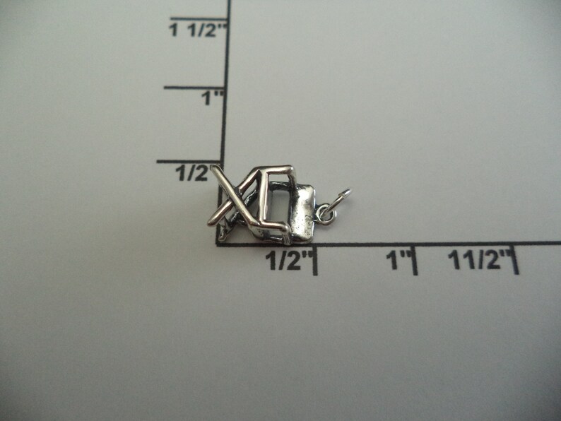May include: A silver charm in the shape of a folding chair. The charm is approximately 1.25 cm tall and 1.25 cm wide. It is a great addition to any charm bracelet.