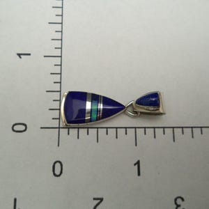 May include: A silver pendant featuring a blue and white stone inlay. The pendant is shaped like a teardrop and has a silver bail.
