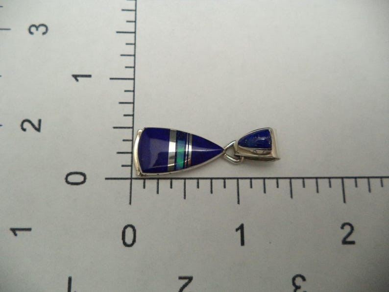 May include: A silver pendant featuring a blue and white stone inlay. The pendant is shaped like a teardrop and has a silver bail.