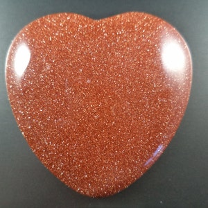 May include: A heart-shaped polished stone with a reddish-brown color and a glittery texture.