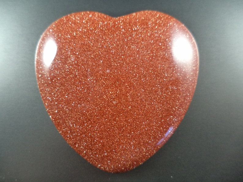 May include: A heart-shaped polished stone with a reddish-brown color and a glittery texture.