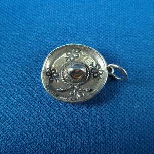 May include: A silver charm in the shape of a sombrero. The charm has a detailed design with a band and a flower pattern.