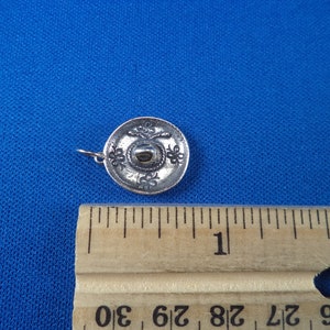 May include: A silver charm in the shape of a sombrero. The charm is about 1 inch in diameter and has a detailed design.