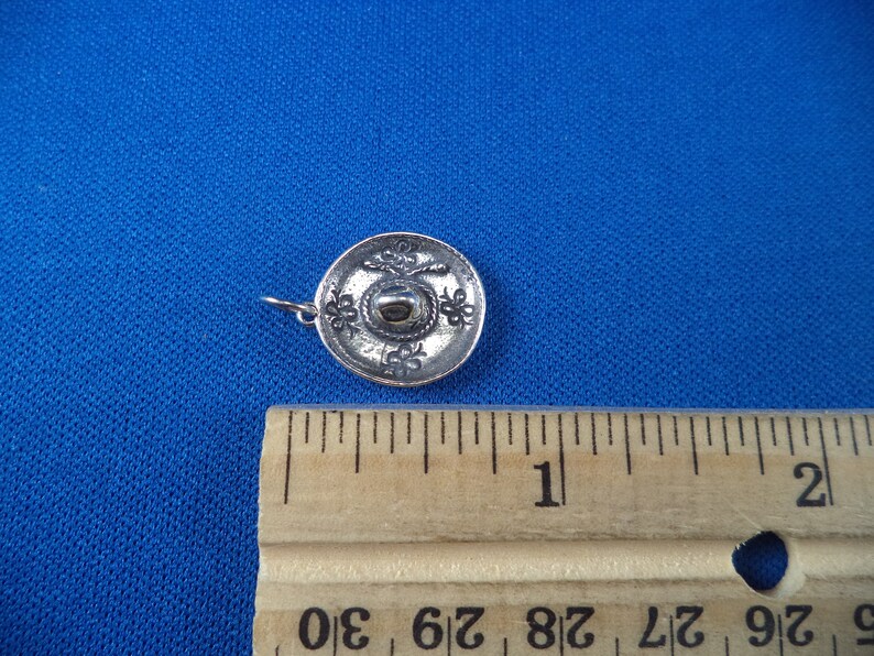 May include: A silver charm in the shape of a sombrero. The charm is about 1 inch in diameter and has a detailed design.