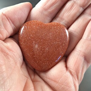 May include: A heart-shaped polished stone with a reddish-brown color and a sparkly, glittery texture.