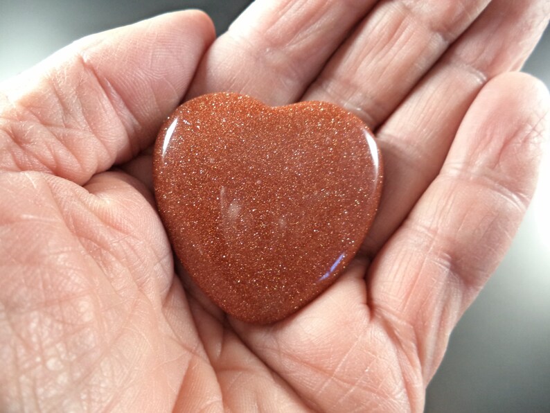 May include: A heart-shaped polished stone with a reddish-brown color and a sparkly, glittery texture.