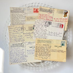 May include: A collection of vintage postcards, some with handwritten messages and stamps, arranged on a clear, decorative glass plate. The postcards feature travel destinations and personal correspondence, evoking nostalgia.