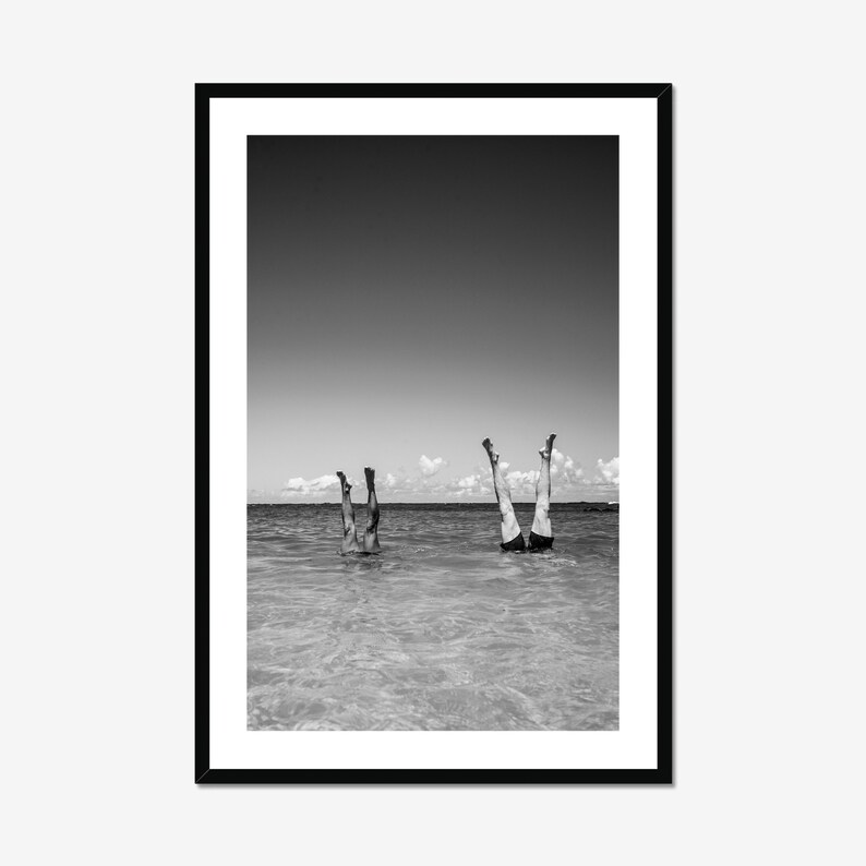 Black and white coastal beach photo print in sleek black frame, vertical wall art styled against white wall for beach cottage decor.
