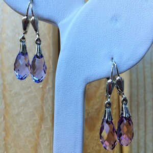 May include: Two pairs of silver dangle earrings with teardrop-shaped purple crystal accents.