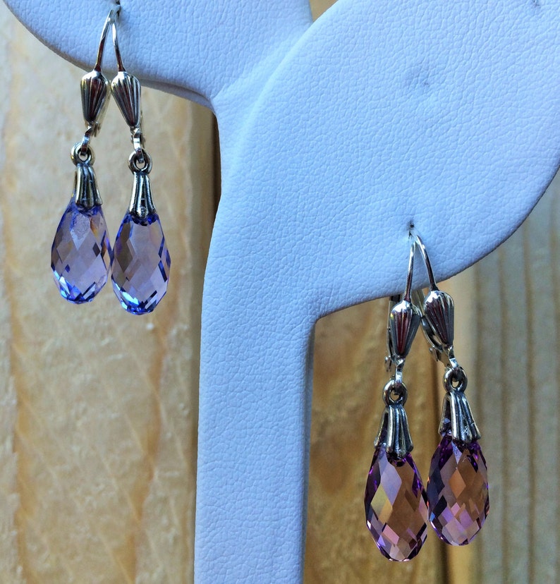 May include: Two pairs of silver dangle earrings with teardrop-shaped purple crystal accents.