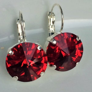 May include: A pair of silver earrings with red crystal stones. The earrings have a lever back closure.