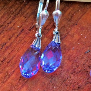 May include: A pair of silver dangle earrings with teardrop-shaped blue crystal stones.
