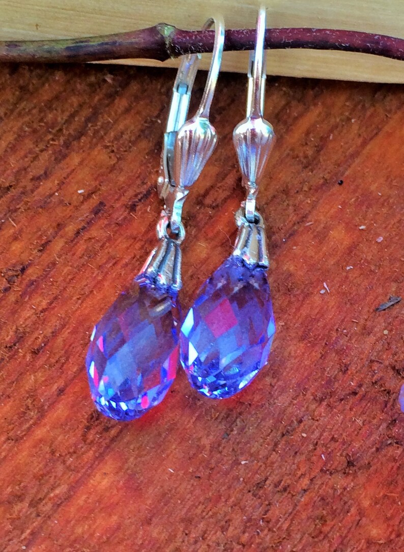 May include: A pair of silver dangle earrings with teardrop-shaped blue crystal stones.