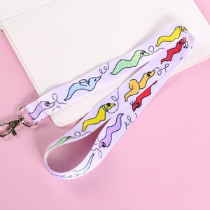 May include: A white lanyard with a repeating pattern of colourful cartoon worms. The lanyard has a silver metal clip.
