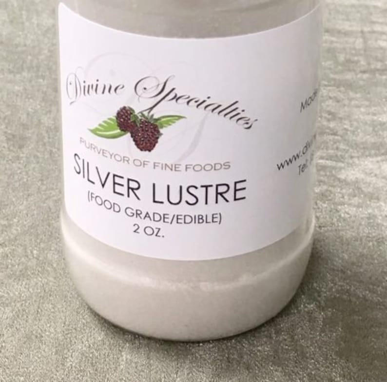 May include: A white jar with a label that reads "Divine Specialties" and "Silver Lustre". The label also states "Purveyor of Fine Foods" and "(Food Grade/Edible)". The jar contains 2 oz of silver luster.
