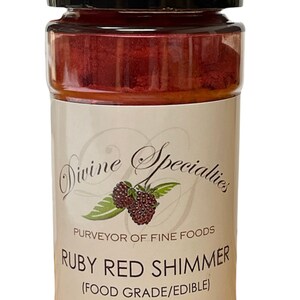 May include: A clear plastic jar with a black lid, filled with ruby red shimmer. The label reads "Divine Specialties" and "Ruby Red Shimmer (Food Grade/Edible) 1 oz."