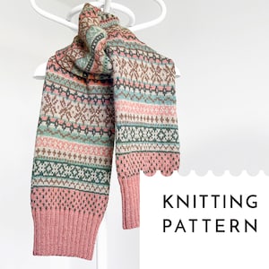 Könnte beinhalten: Ein gestrickter Schal mit einem Muster in Rosa, Braun und Grün. Der Schal ist gefaltet und auf einem weißen Kleiderbügel ausgestellt. Der Text "Knitting Pattern" steht auf einem weißen, gewellten Etikett.