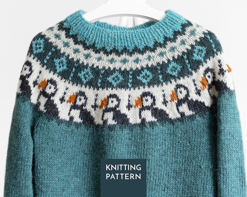 A teal knitted jumper featuring a circular yoke with a fair isle pattern. The design includes rows of geometric shapes in white and dark teal, and a row of stylised puffin birds with white bodies, dark wings, and orange beaks.