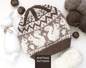 Könnte beinhalten: Eine Strickmütze mit einem Fair-Isle-Muster in Braun- und Cremetönen sowie einem einfarbigen, braunen Rippbündchen. Das Design zeigt wiederkehrende geometrische Formen und stilisierte Tiermotive. Ein dunkles Quadrat zeigt den Text KNITTING PATTERN.